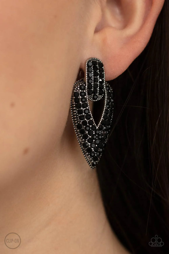 Paparazzi Blinged Out Buckles - Black Clip-On Earrings - The front of a spade shaped silver frame is encrusted in row after row of glittery black rhinestones, creating a blinding buckle inspired statement piece. Earring attaches to a standard clip-on fitting.