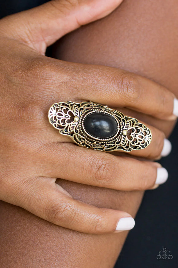 Dotted with an earthy black stone center, glistening brass filigree climbs the finger, coalescing into a dramatic frame. Features a stretchy band for a flexible fit.