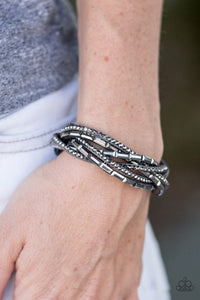 Paparazzi Too Cool For School - Silver - Bracelet  -  A gray strip of suede is spliced into glittery bands braided across the wrist in a sassy fashion. Round hematite rhinestones and emerald-cut hematite beading create the ultimate collision of sparkle. Features an adjustable snap closure.
