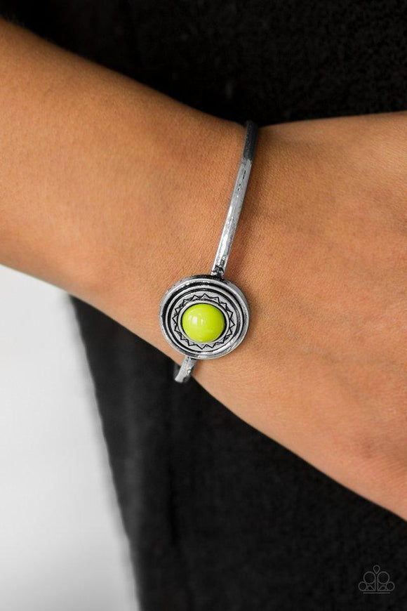 Paparazzi Sahara Sunshine - Green A vivacious green bead is pressed into the center of a dainty silver frame radiating with a sunburst pattern, creating a seasonal cuff around the wrist.

