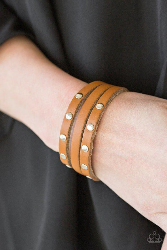 Paparazzi Radical Raider - Brown A shiny brown leather band is spliced into three strands. Flat silver beads are studded down the outer strands, adding a rugged finish to the urban palette. Features an adjustable snap closure.

