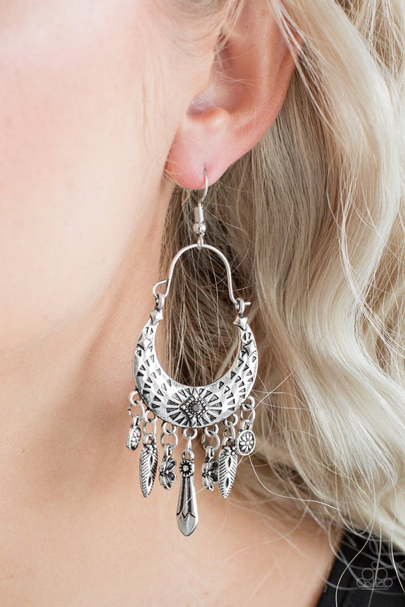 Paparazzi Nature Escape - Silver - Earrings  -  Stamped in triangular textures, a shimmery silver crescent frame gives way to a fringe featuring glistening floral and abstract charms. Suspended by a dainty wire fitting, the tribal inspired frame is dotted with a dainty hematite rhinestone for a sparkling finish. Earring attaches to a standard fishhook fitting.
