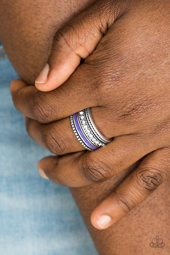 Paparazzi Rich Rogue - Purple A vivacious purple strip of color runs along the bottom of a row of glassy white rhinestones. Infused with silver textures, the mismatched details coalesce into one thick band across the finger. Features a stretchy band for a flexible fit

