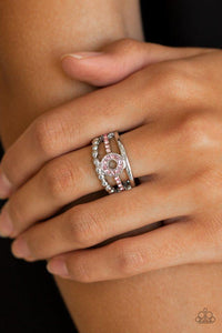 Paparazzi Cost of Living - Pink A smooth and dotted silver band flank a pink rhinestone encrusted band, creating glittery layers across the finger. Encrusted in glassy pink rhinestones, a circular frame is pressed into the center of the bands for a refined finish. Features a dainty stretchy band for a flexible fit.

