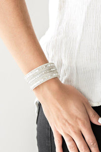Paparazzi Rebel Radiance - White  -  Featuring classic round and edgy emerald style cuts, glittery white rhinestones and glistening silver chains are encrusted along bands of white suede for a sassy look. Features an adjustable snap closure.
