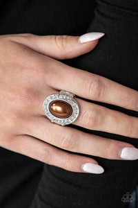 Paparazzi The ROYALE Treatment - Brown A pearly brown bead is pressed into a silver oval frame radiating with a ring of glittery white rhinestones, creating a regal statement piece atop the finger. Features a stretchy band for a flexible fit.

