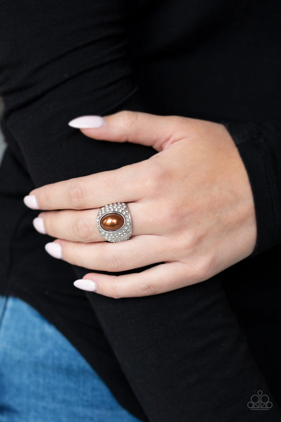 Paparazzi Glittering Go-Getter - Brown A pearly brown bead is pressed into the center of a bold silver band radiating with countless white rhinestones, creating a dramatic statement piece atop the finger. Features a stretchy band for a flexible fit.
