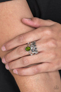 Paparazzi Crowned Victor - Green Three glistening silver bars arc across the finger, coalescing into a layered band. A glittery green gem crowns the uppermost band, while emerald-cut hematite rhinestones are encrusted along the lowermost band for a regal look. Features a stretchy band for a flexible fit.
