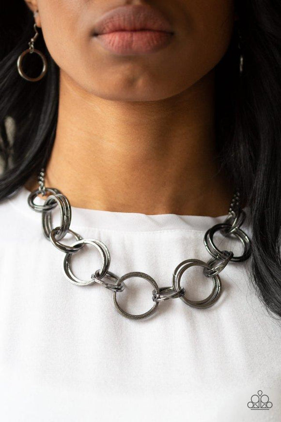 Paparazzi Jump Into The Ring - Black  -  Brushed in an antiqued shimmer, doubled and tripled gunmetal hoops link below the collar for a bold industrial look. Features an adjustable clasp closure.
