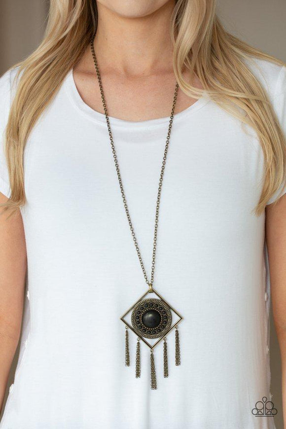 Paparazzi Sandstone Solstice - Brass  -  Radiating with studded details and earthy black stones, a round frame is nestled inside of an airy brass square for a tribal inspired look. Attached to a lengthened brass chain, the colorful stone pendant gives way to rows of brass chain fringe for a statement-making finish. Features an adjustable clasp closure.
