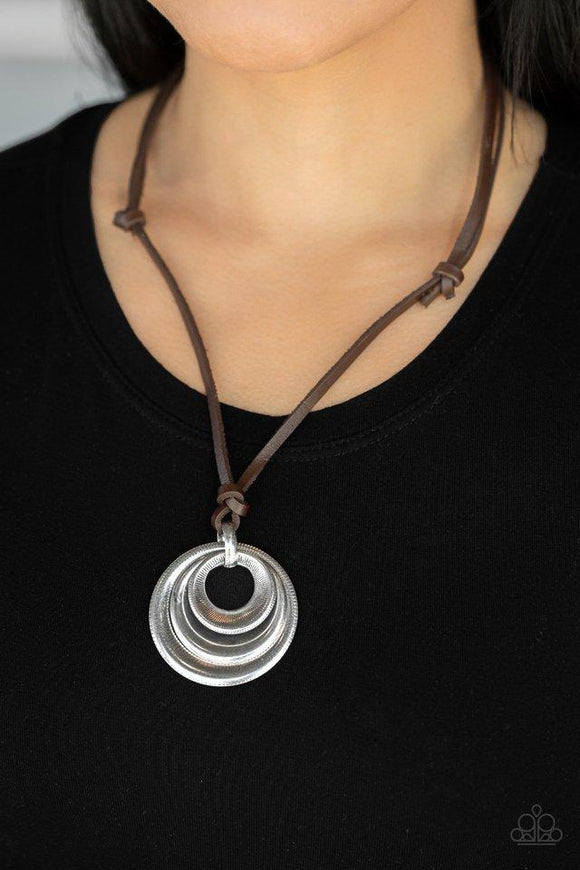 Paparazzi Desert Spiral - Silver  -  Textured and smooth beveled silver rings are knotted in place at the bottom of a brown leather cord, creating a rustic pendant. Features an adjustable sliding knot closure.
