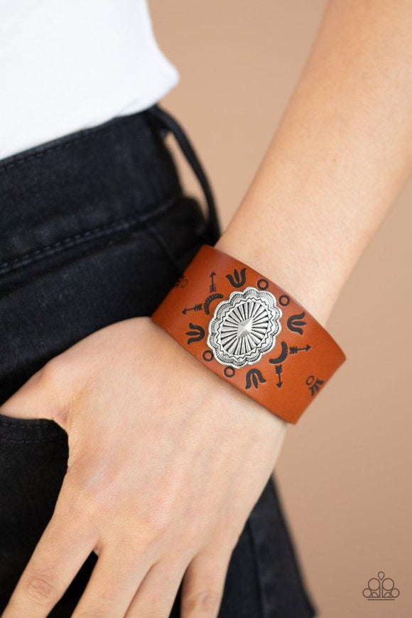 Paparazzi Desert Badlands - Brown  -  An ornate silver frame is pressed into the center of a rust brown leather band stamped in desert inspired glyphs for a seasonal flair. Features an adjustable snap closure.
