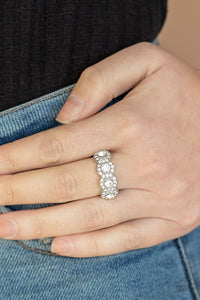 Paparazzi Ever Enlightened - White - Ring  -  Bordered in rings of dainty white rhinestones, four classic white rhinestones are encrusted along the front of a dainty silver band for a timeless shimmer. Features a dainty stretchy band for a flexible fit.
