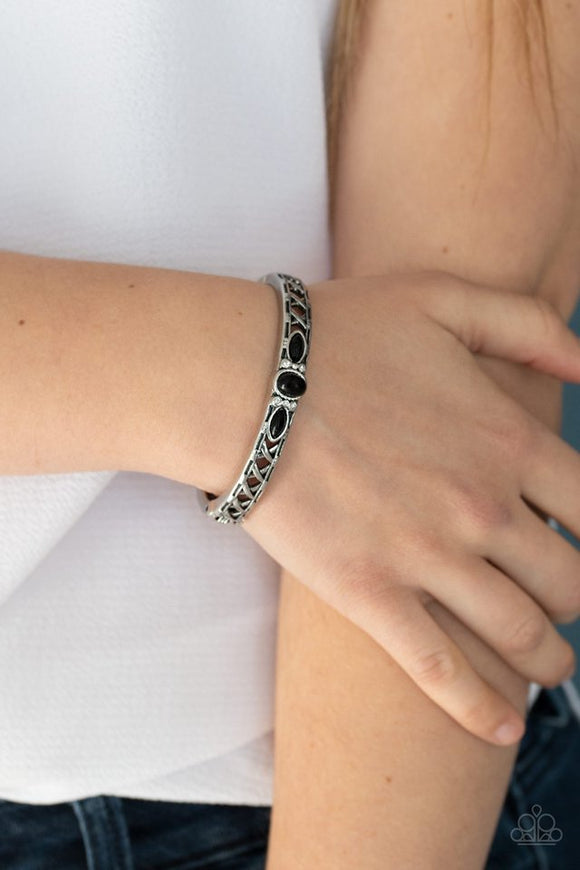 Paparazzi Caught In The Cross HEIRS - Black - Bracelet  -  Dotted with a black beaded and glassy rhinestone encrusted centerpiece, a crisscrossing silver bangle-like cuff slides along the wrist for a whimsical look. Features a hinged closure.
