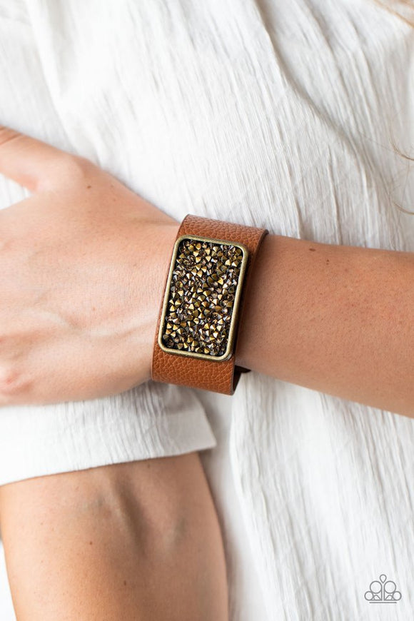 Paparazzi Interstellar Shimmer - Brass - Bracelet  -  A collision of topaz and aurum rhinestones collect inside a brass rectangular frame that is studded in place in the center of a thick brown leather band, creating a sparkling statement piece around the wrist. 
