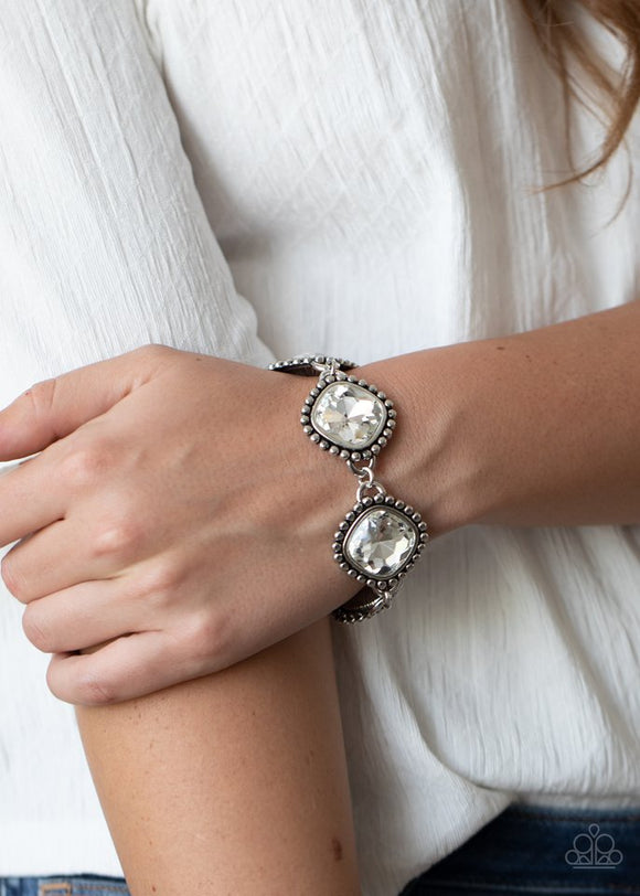 Paparazzi Megawatt - White - Bracelet  -  Featuring dramatically studded silver frames, an exaggerated display of oversized white rhinestone encrusted frames delicately link around the wrist for a blinding look. Features an adjustable clasp closure.
