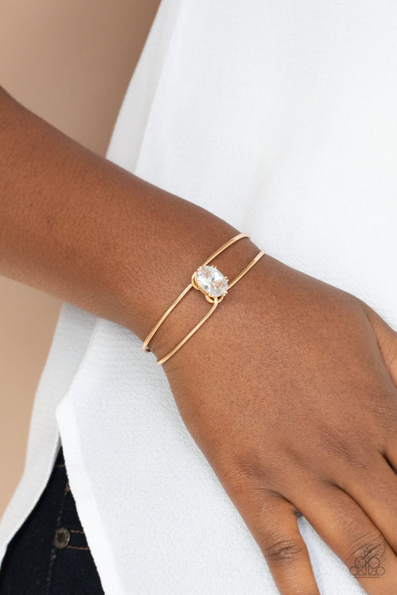Paparazzi GLOW No Mercy - Gold - Bracelet   -  A dramatically oversized white rhinestone is fitted in place atop the center of a gold wire cuff, creating a jaw-dropping display around the wrist.
