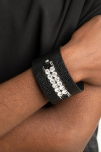 Paparazzi Runway Rebellion - Black - Bracelet  -  Two rows of oversized white rhinestones are studded in place across the center of a thick black leather band, creating a sassy centerpiece around the wrist. Features an adjustable snap closure.
