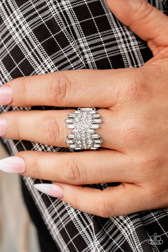 Paparazzi Urban Empire - White - Ring  -  Staggered rows of emerald cut rhinestones flare out from the top and bottom of an explosion of classic white rhinestones, creating a smoldering statement piece atop the finger. Features a stretchy band for a flexible fit.

