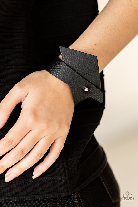 Paparazzi PIECE Offering - Black - Bracelet   -  A triangular piece of black leather delicately wraps around the wrist, creating an edgy asymmetrical centerpiece around the wrist. Features a studded button loop closure.
