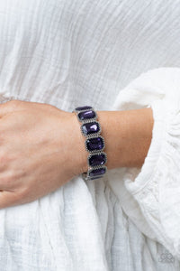 Paparazzi Studded Smolder - Purple - Bracelet  -  Oversized emerald style purple gems are encased in antiqued studded frames that are threaded along stretchy bands around the wrist, creating a smoldering centerpiece.
