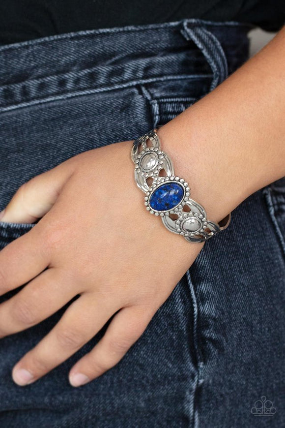 Paparazzi Solar Solstice - Blue - Bracelet  -  An oval blue stone is pressed into the center of a studded silver frame atop an airy silver cuff embellished in studded sun-like frames for an earthy pop of seasonal color around the wrist.
