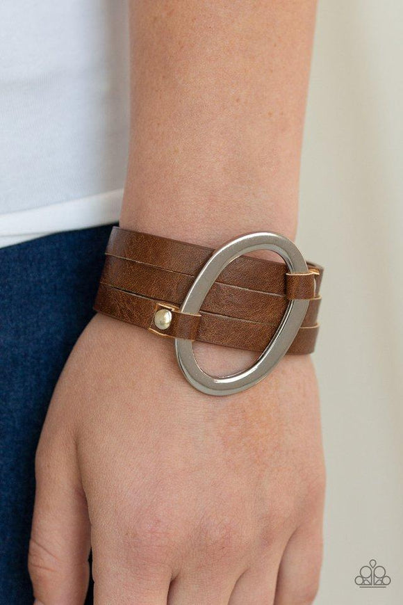 Paparazzi Cowgirl Cavalier - Brown - Bracelet
An oval silver ring loops through two belt loop fittings and is studded in place across the front of a spliced brown leather band for a bold urban look. Features an adjustable snap closure. 
