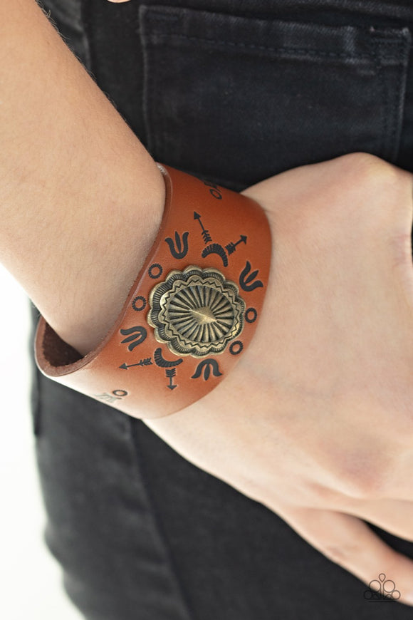 Paparazzi Desert Badlands - Brass - Bracelet
An ornate brass frame is pressed into the center of a rust brown leather band stamped in desert inspired glyphs for a seasonal flair. Features an adjustable snap closure.
